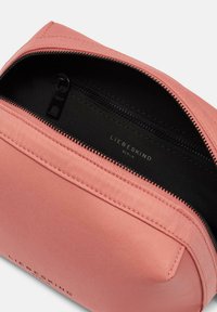 Rosa kosmetische Tasche aus Stoff mit Reißverschluss. Innenausstattung mit schwarzem Futter und einem Etikett "LIEBESKIND BERLIN." Glatte Textur und abgerundete Form.