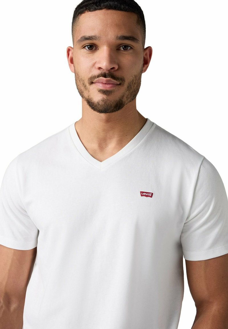 Mann mit kurzen Haaren und Bart trägt ein weißes Levi's T-Shirt mit V-Ausschnitt vor einem schlichten weißen Hintergrund.