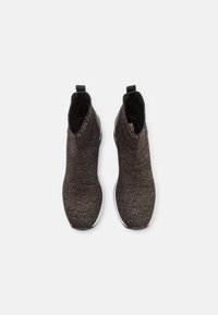 Bottes chelsea en tricot noires et dorées à coupe basse avec un ajustement en forme de chaussette, texture lisse et semelle en caoutchouc noir. Dispose d'une languette au niveau du talon.
