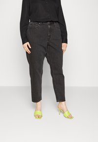 Hoch-taillierte schwarze Denim-Jeans mit schmal zulaufendem Bein, kombiniert mit limonengrünen Absatzsandalen mit einem gesteppten Riemendesign.