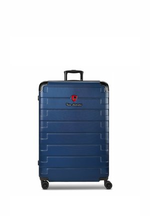Blauwe harde koffer met vier wielen, een zwart uitschuifbaar handvat en een rood logo vlakbij het bovenste midden.
