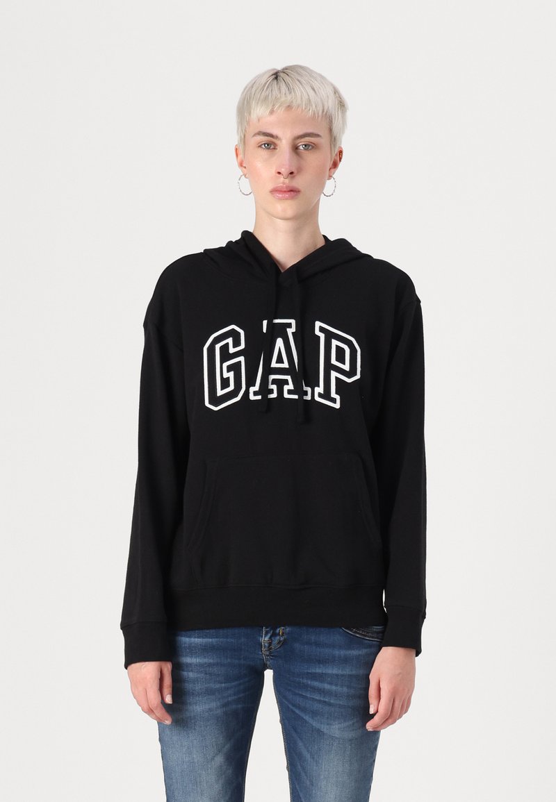 Black hooded sweatshirt with white "GAP" logo, front kangaroo pocket, long sleeves, and ribbed hem. Worn with blue jeans.