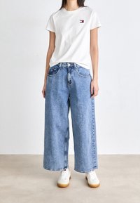 Vit bomullströja med liten logotyp, kombinerad med högmidjade, vida blå denimjeans. Vita sneakers med gummisulor.