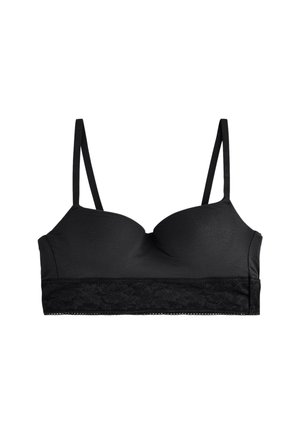 Femme portant un bralette noir avec des bretelles fines et des détails en dentelle sous la poitrine, vue de profil et recadrée aux épaules.