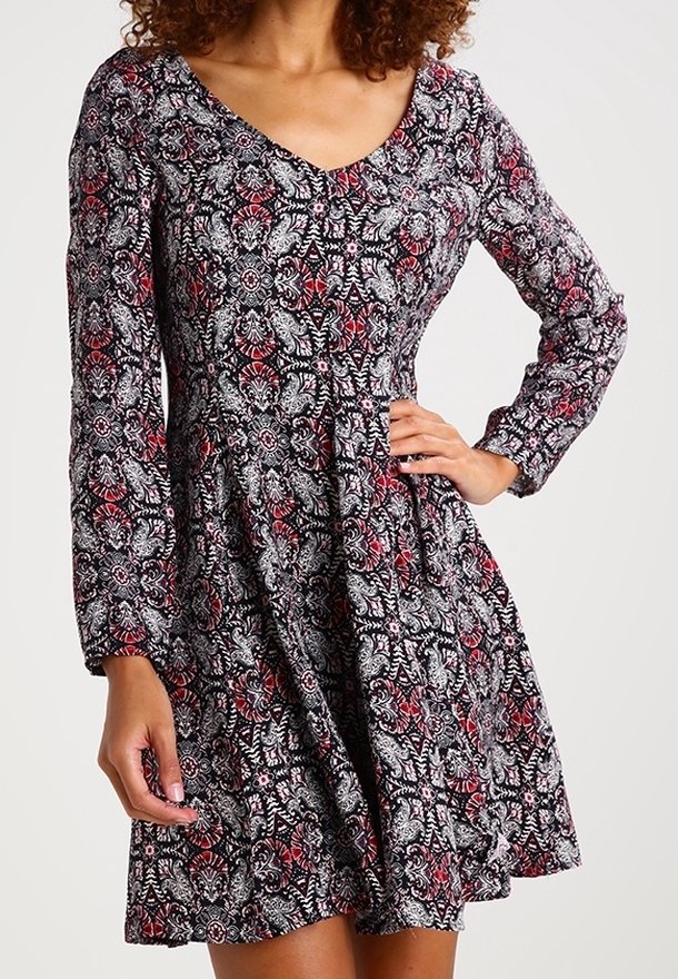 Abito floreale in bianco e nero con maniche lunghe, scollo a V e gonna svasata; presenta dettagli rossi e un tessuto leggero e testurizzato.