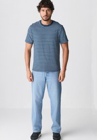 Camiseta de rayas azules y blancas de manga corta con cuello redondo, combinada con unos jeans de pierna recta de color azul claro y zapatillas negras.