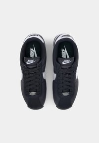 Černé a šedé tenisky Nike s texturovaným textilním svrškem, šněrováním, stříbrnými akcenty a pevným černým gumovým podešví.