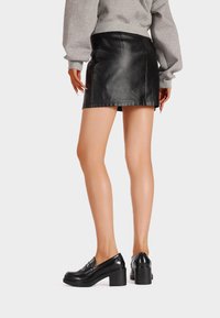 Mini gonna in pelle nera con design elegante, caratterizzata da una texture liscia e cuciture in vista. Abbinata a scarpe con tacco a blocco nere.