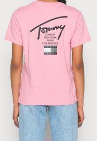Różowa bawełniana koszulka z dużym czarnym logo z napisem "Tommy" oraz nazwami miast, dodatkowo z metką "Tommy Jeans" poniżej w prostokątnym wzorze.