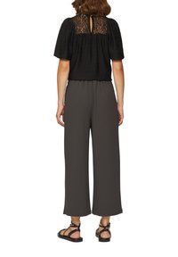 Zwarte top met kant achteraan, gecombineerd met wijde charcoal broek en zwarte gespsandalen. Gladde textuur, relaxed fit, casual stijl.