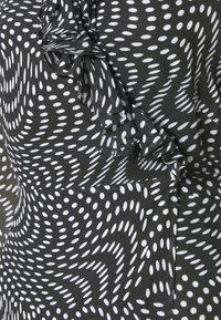 Zwarte stof met witte langwerpige polkadots, gerangschikt in wervelende patronen en een diagonaal gerimpeld naaddetail.