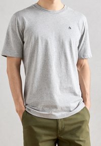 Grijze t-shirt met korte mouwen van katoen. Heeft een ronde halslijn en een klein geborduurd logo op de linkerborst. Zachte textuur.