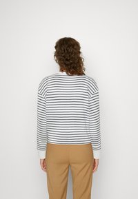 Maglione a righe in bianco e blu navy, texture a coste, design corto, presenta maniche lunghe e un collo rotondo, abbinato a pantaloni beige.