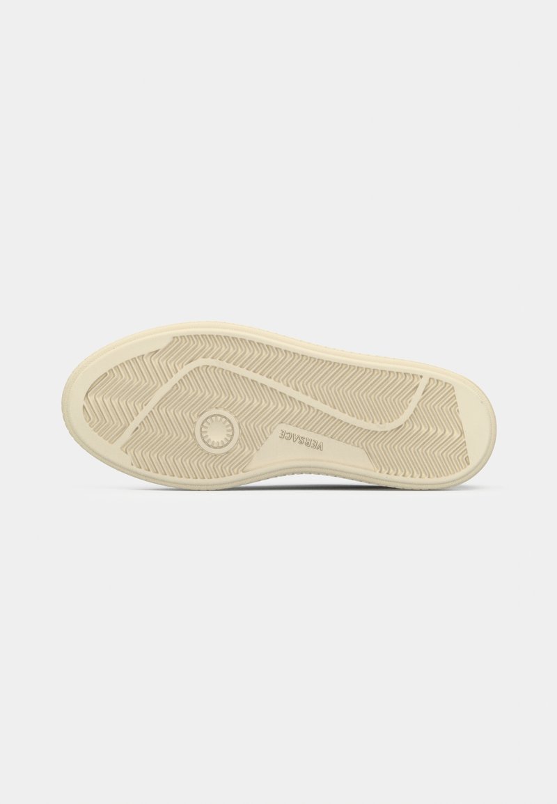 Sole of a sneaker with a textured design, featuring a cream color and rubber material, showing traction patterns and a circular logo.
