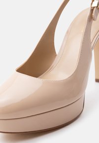 Πλατφόρμα ψηλοτάκουνο παπούτσι από μπεζ δερμάτινο γυαλιστερό δέρμα με λουρί στο πίσω μέρος και στρογγυλεμένη μύτη σε λευκό φόντο.