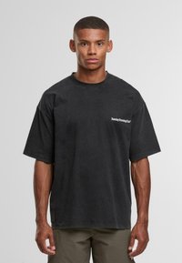 Černé oversized bavlněné tričko s krátkým rukávem a kulatým výstřihem, s bílým tištěným logem v oblasti levého horního prsou.