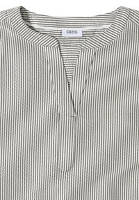 Chemise à rayures verticales blanches et grises avec un col rond et une petite fente à l'avant, étiquette "CECIL" à l'intérieur du col.