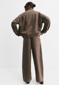 Veste oversize en coton marron avec un pantalon large assorti. Le design présente des coutures visibles et deux poches arrière sur le pantalon.
