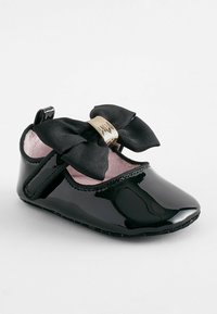Schwarzer Lackleder Babyschuh mit runder Zehenform, ausgestattet mit einer großen schwarzen Schleifenbinde und einem goldenen metallischen Akzent, gefüttert mit pinkem Stoff.