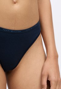 Granatowa bawełniana bielizna bikini z logo w pasie, na którym znajduje się napis "TOMMY HILFIGER", oferująca gładki i dopasowany krój.