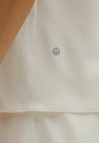 Gros plan sur un tissu athlétique blanc texturé avec le logo Lululemon au-dessus d'un matériau perforé blanc.