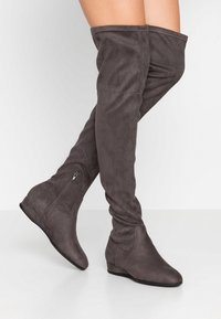 Botas sobre la rodilla de ante gris con un diseño arrugado, puntera afilada y cremallera lateral para facilitar su uso. Tacón bajo en cuña.