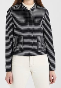 Marynarka w paski w kolorach granatowym i białym, z okrągłym dekoltem, dwoma przednimi kieszeniami oraz krótkim fasonem i długimi rękawami. Miękka, elastyczna tkanina.