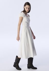 Vestido blanco de mangas abullonadas con un torso ajustado y falda acampanada, combinado con botas negras hasta la rodilla con hebillas y tacón bajo.