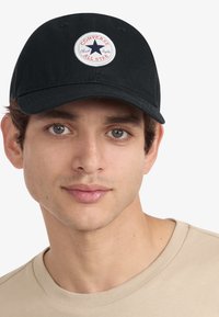 Gorra negra de algodón con visera redondeada, que presenta un parche circular rojo y blanco con una estrella azul y el logotipo "Converse All Star".