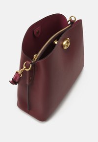 Sac à main en cuir rouge foncé avec quincaillerie dorée, rabat ouvert et compartiment central zippé, présenté en angle sur un fond blanc.