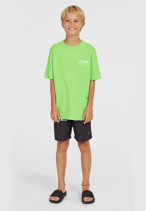 Lys grøn kortærmet t-shirt med hvidt logo, parret med sorte badebukser. Materialet ser let ud; sandalerne er sorte med flade såler.