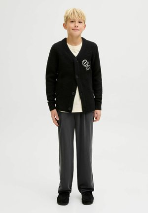 Cardigan nero a maglia con finitura testurizzata, dotato di scollatura a V, chiusura con bottoni e lettere ricamate bianche. Abbinato a pantaloni grigi.