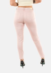 Pantalones ajustados rosa con una textura suave, cinco bolsillos y una discreta etiqueta de la marca en la cinturilla. Combinados con tacones altos negros.