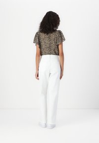 Kort topp med leopardtryck, utsvängda ärmar; i kombination med hög midja, raka vita byxor; modell som bär vita sneakers.