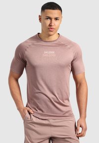 Camiseta deportiva de color rosa claro, con mangas cortas, tejido texturizado y un logo sutil en el pecho. Combinada con shorts de color beige claro.