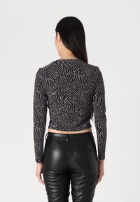 Musta pitkähihaine paita, jossa on metalliset raidat ja seeprahihenkäyte. Lyhennetty malli, tiukka siluetti ja pyöreä kaula-aukko. Yhdistetty mustiin nahkahousuihin.