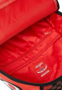 Interior rojo de una mochila que presenta un bolsillo de malla, una sección con cremallera y una etiqueta incrustada en la tela, con una textura suave.