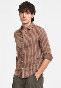 Camicia a righe marroni con bottoni, realizzata in tessuto leggero, dotata di colletto, maniche arrotolate e bottoni bianchi per la chiusura.