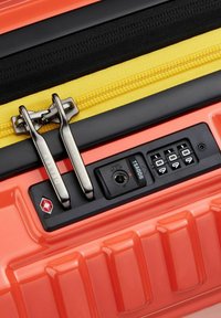 Maleta rígida naranja con tiradores de cremallera de metal dobles, cremallera de tela amarilla y cerradura de combinación aprobada por la TSA incorporada.