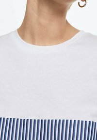 Camiseta blanca de manga corta con un patrón de rayas horizontales azules y blancas en la mitad inferior y un cuello redondo.
