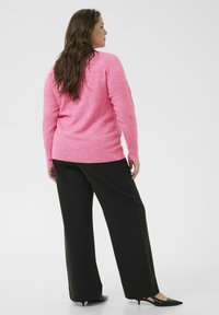 Ružový pletený sveter s dlhými rukávmi, skombinovaný s širokými čiernymi nohavicami a čiernymi lodičkami na podpätku. Hladká textúra a ležérny dizajn.