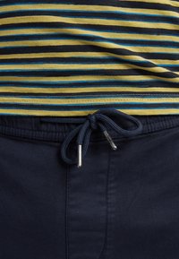 Pruhovaná košile se žlutými, černými a modrými vodorovnými pruhy, spárovaná s námořnicky modrými kalhotami s tkaničkou a stříbrným kováním.