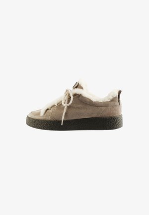 Brun ruskind sneaker med hvid fleeceforing, beige snørebånd og sort struktureret sål, vist fra siden på en hvid baggrund.