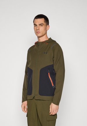 Green zip-up jacket with a black panel, featuring orange zipper accents and hood, made from lightweight material, ideal for outdoor use.