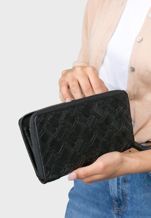 Portafoglio in pelle intrecciata nera con chiusura a zip, caratterizzato da un motivo testurizzato. Tenuto da una mano, che ne mostra la forma rettangolare e il profilo sottile.