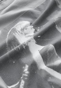 T-shirt en tissu gris avec une photo imprimée en noir et blanc d'une personne, présentant des textures et des plis visibles dans le matériau.