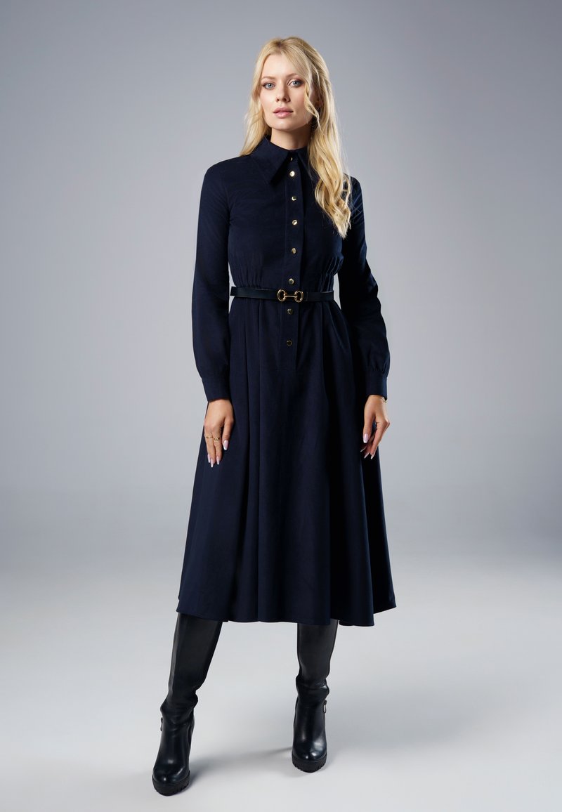 Granatowa sukienka z długim rękawem, z guzikami z przodu, wcięciem w talii, paskiem z złotymi akcentami oraz zwiewną spódnicą, zestawiona z czarnymi kozakami za kolano.