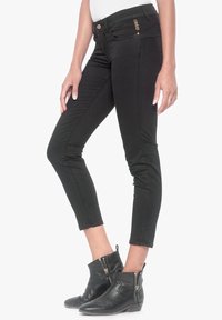 Černé denimové džíny s úzkým střihem, zkrácenou délkou a zipovým detailem na kotníku. Disponují zlatým knoflíkem a švy jako ozdobnými prvky.