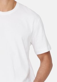 Weißes Baumwoll-T-Shirt mit Rundhalsausschnitt, kurzen Ärmeln und einer weichen, glatten Textur. Der Stoff wirkt leicht und atmungsaktiv.