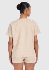 Vaurio beige t-paita lyhyillä hihoilla, jossa on teksturoitu kangas, pyöreä pääntie ja rento istuvuus. Yhdistettynä matching shortseihin, katsottuna takaa.